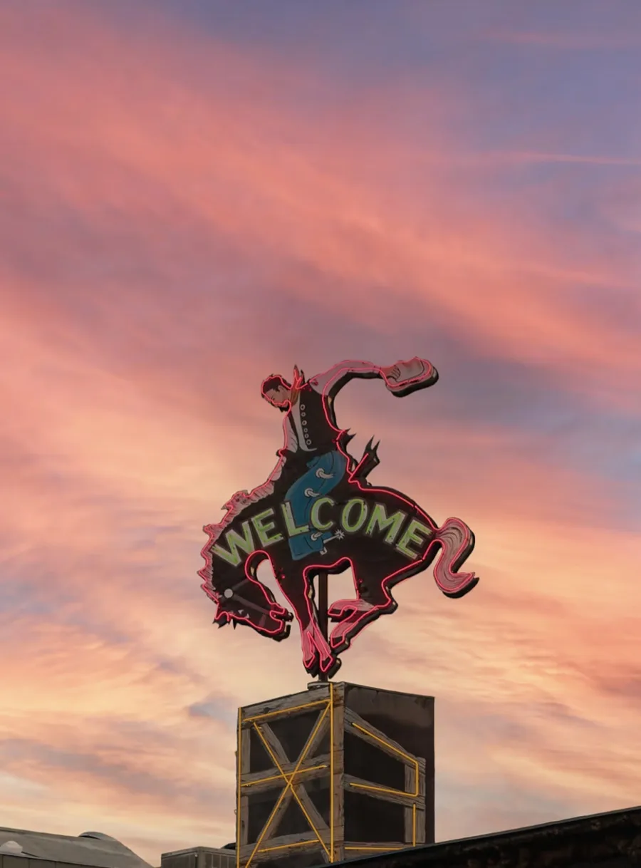 A neon bucking-horse sign reading Welcome against a sunset sky